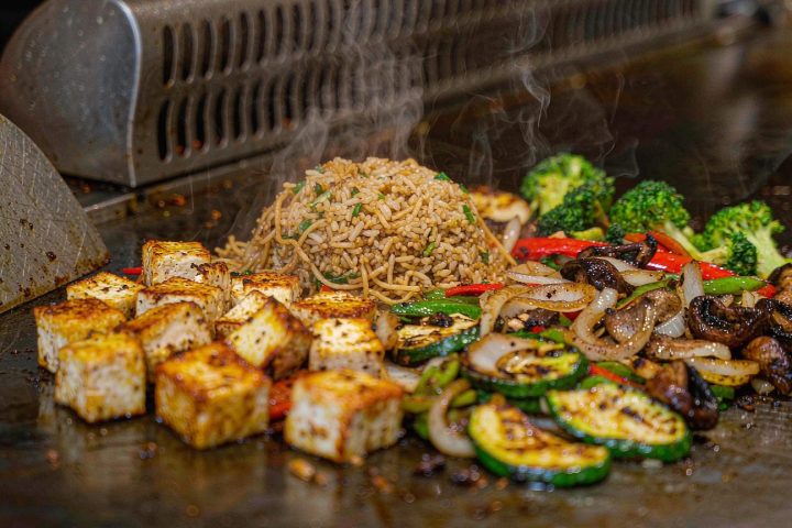 Grilled tofu and vegetables with hibachi fried rice cooking on a teppanyaki flat-top grill